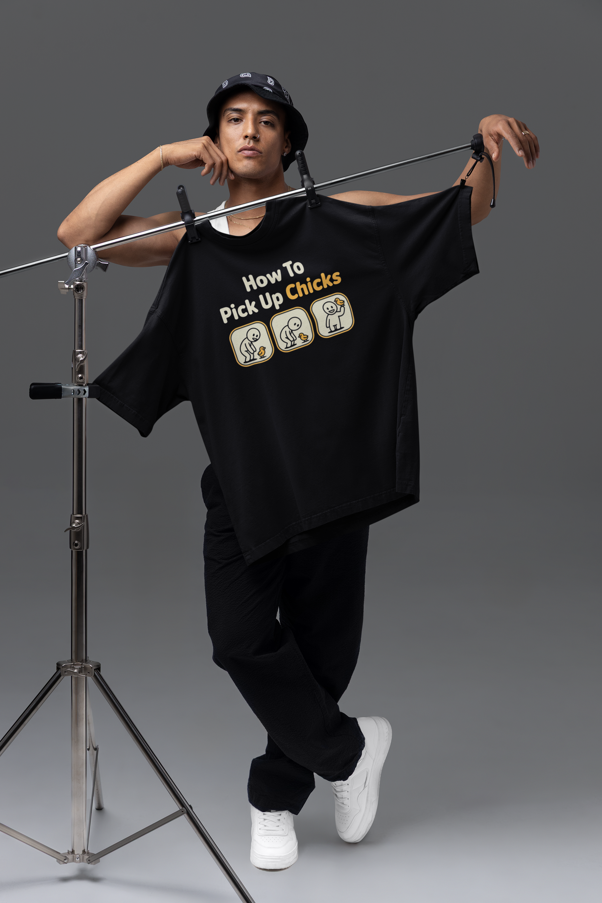 Person wearing a black t-shirt with text and graphics, standing next to a microphone stand on a gray background