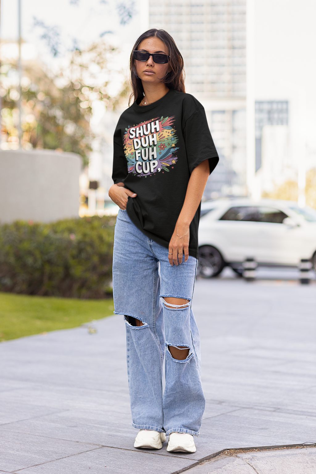 Person wearing a black t-shirt with colorful text and ripped jeans on a city street.