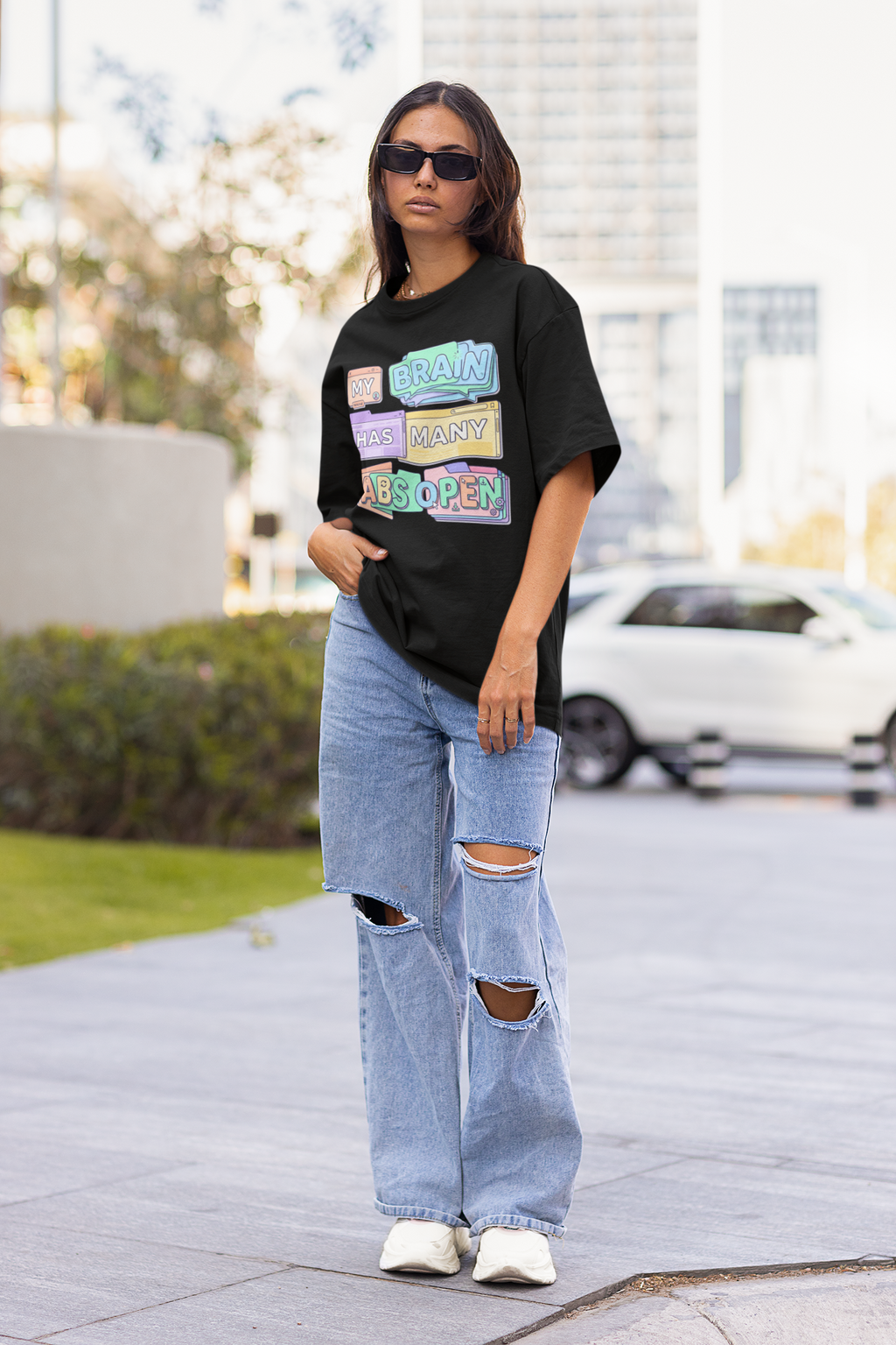 Person wearing a black graphic t-shirt and ripped jeans on a city street.