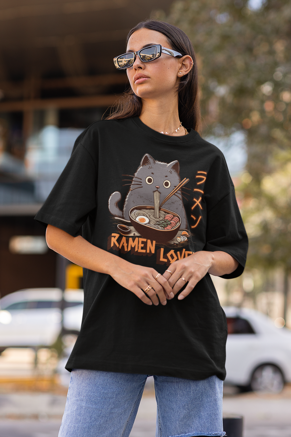 Person wearing a black t-shirt with a cat and ramen design outdoors.