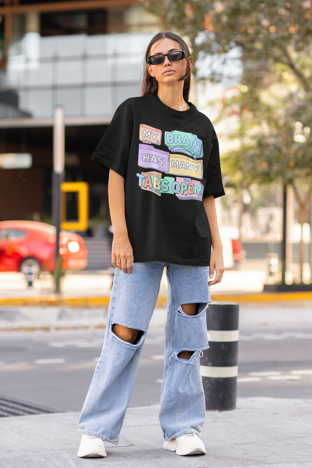 Person wearing a black oversized t-shirt with colorful text and ripped jeans on a city street.