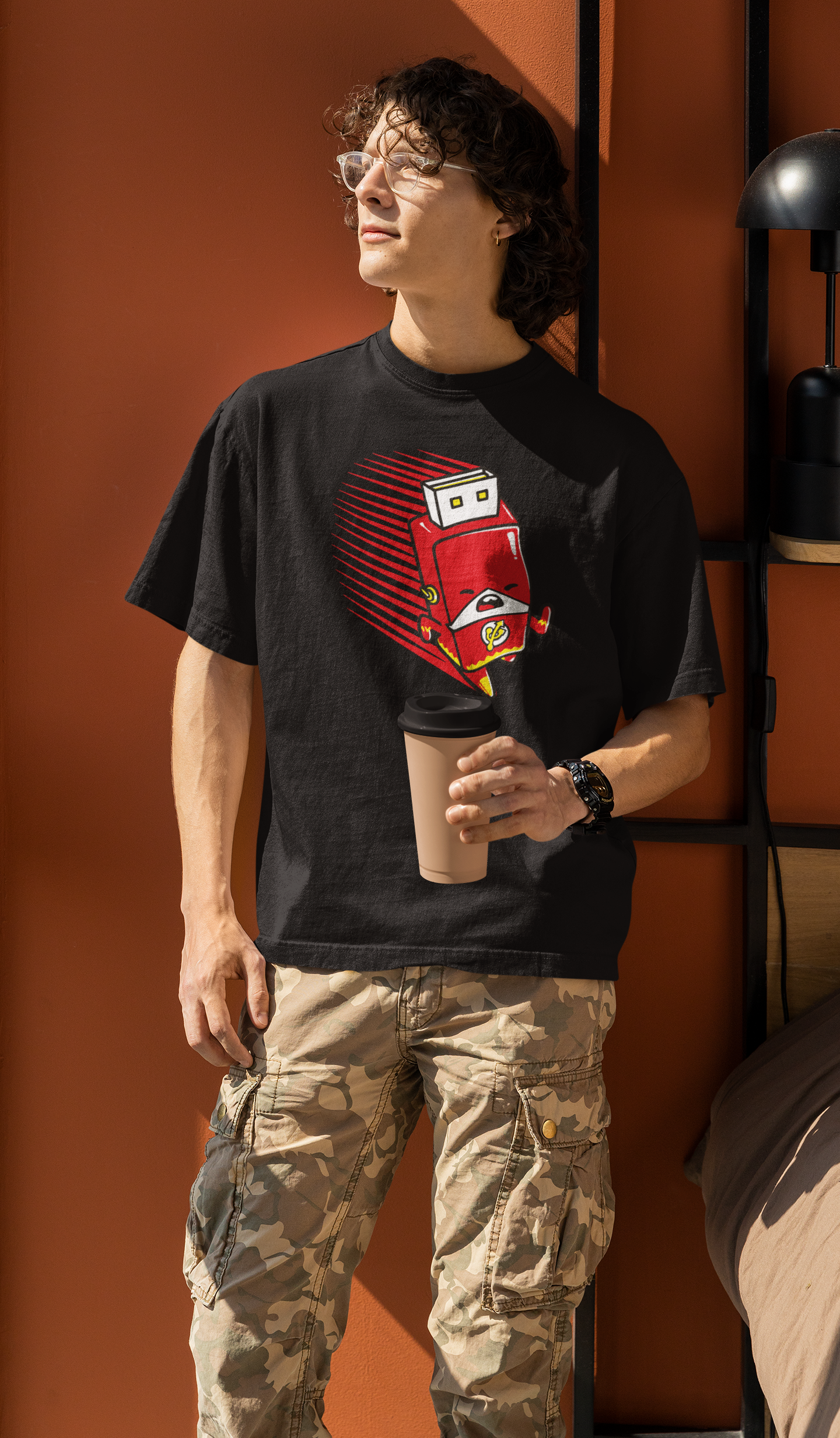 Person wearing a black t-shirt with a red graphic design, standing against an orange wall.