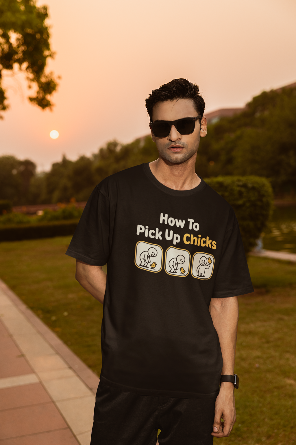 Man wearing a black t-shirt with humorous text and graphics outdoors during sunset.