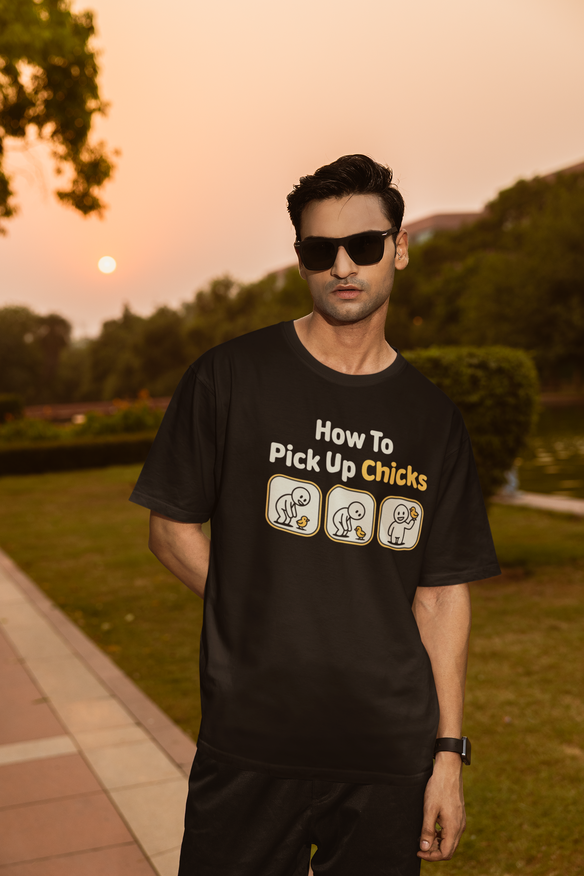 Man wearing a black t-shirt with humorous text and graphics outdoors during sunset.