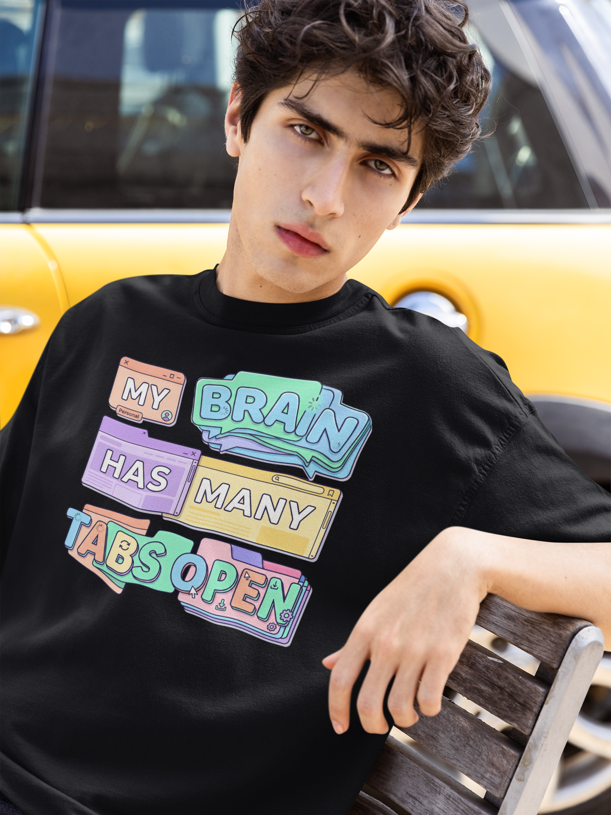 Person wearing a black t-shirt with colorful text design, sitting on a bench.