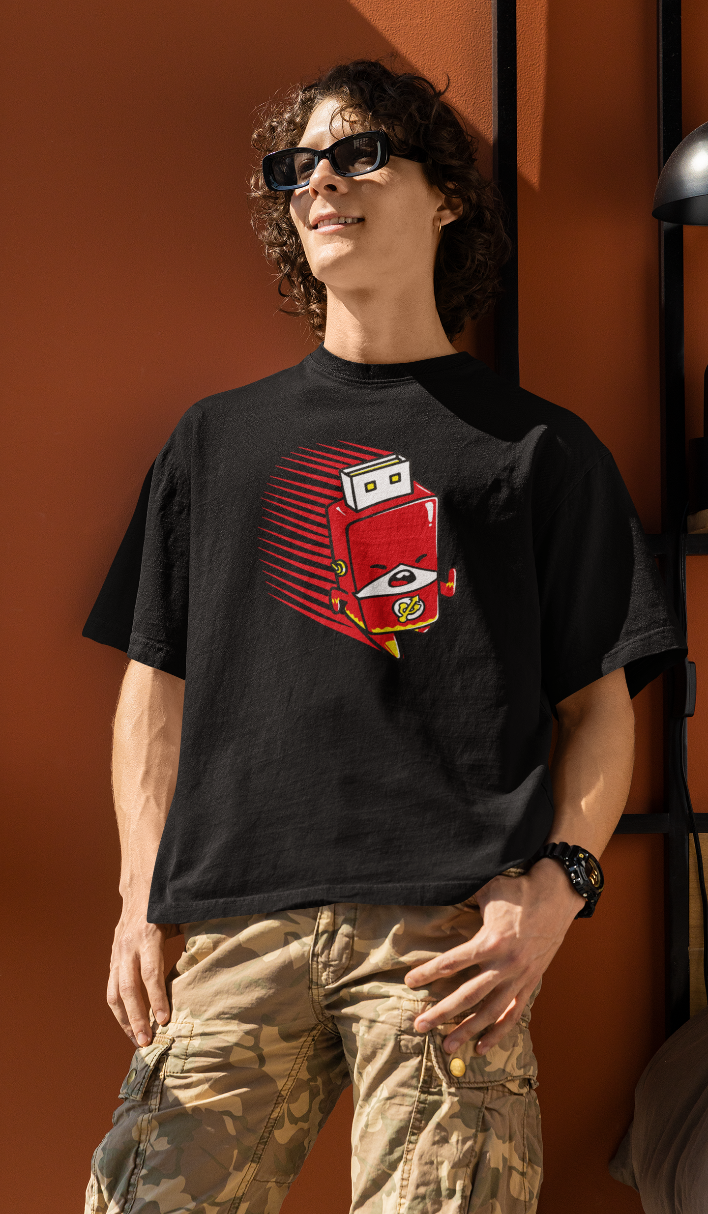 Person wearing a black t-shirt with a red graphic design, standing against an orange wall.