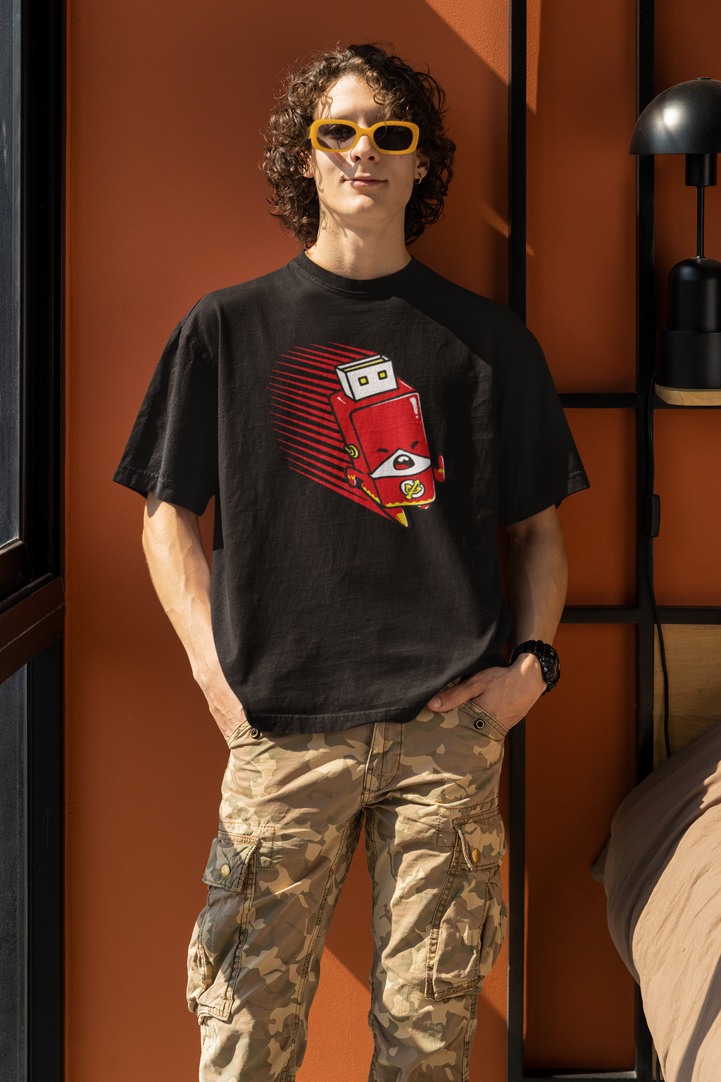 Person wearing a black t-shirt with a red graphic design, standing against an orange wall.